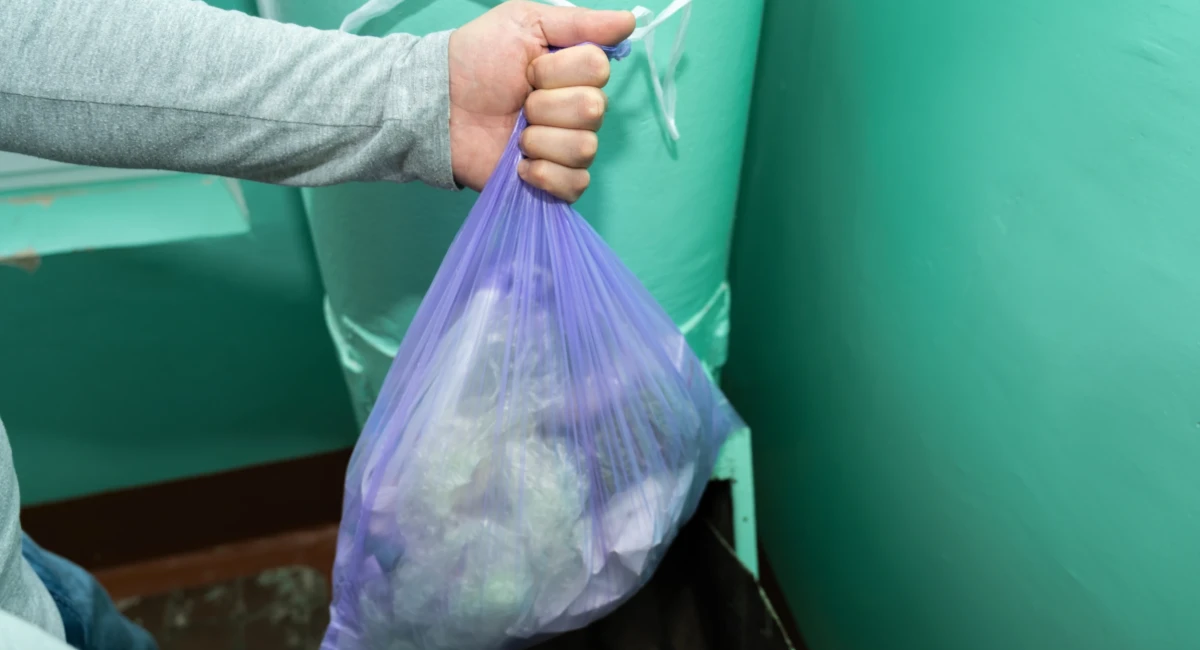 A man putting a garbage bag into a dumpster
