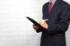 A person in a suit writing on a clipboard.
