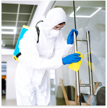 A person dressed in full-body protective gear cleaning a door handle with a sponge.