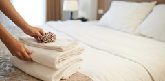 A hotel staff member setting a pile of towels on a bed.