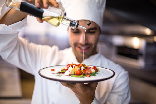 A chef garnishes a dish with olive oil.